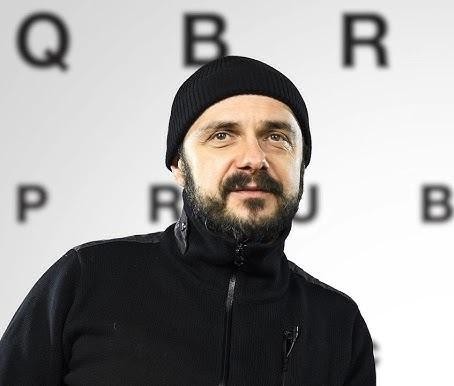 Arkadiusz Jakubik, wokalista zespołu Dr Misio, podczas energicznego występu na scenie, śpiewający do mikrofonu, w dynamicznej pozie.