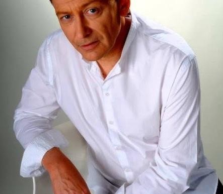 Jacek Borkowski na scenie teatralnej, w trakcie występu, oświetlony reflektorami.