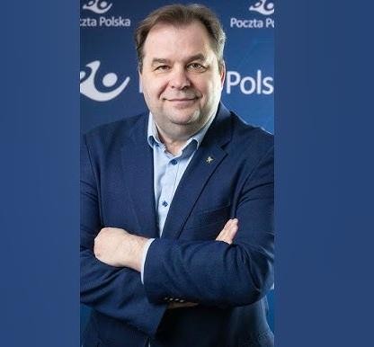 Portret Sebastiana Mikosza w garniturze w biurze, symbolizujący jego rolę menedżera i prezesa Poczty Polskiej, z elementami nawiązującymi do branży lotniczej.