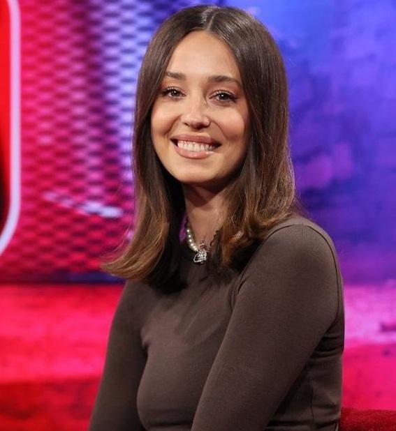 Izabella Krzan podczas pracy jako prezenterka telewizyjna, trzymająca mikrofon na tle studia TV.
