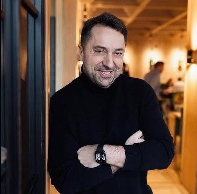 Marcin Miller uśmiechnięty, z optymizmem patrzący w obiektyw, na delikatnie rozmytym tle.