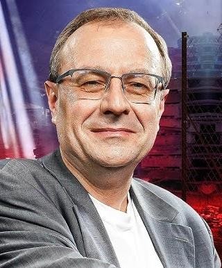Antoni Dudek podczas wykładu lub prezentacji, dynamicznie gestykulujący, w tle z elementami nawiązującymi do historii lub mediów.