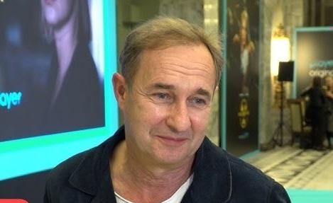 Marek Kalita na scenie teatralnej, w dynamicznej pozie, otoczony subtelnym oświetleniem scenicznym, oddający esencję swojej scenicznej obecności.