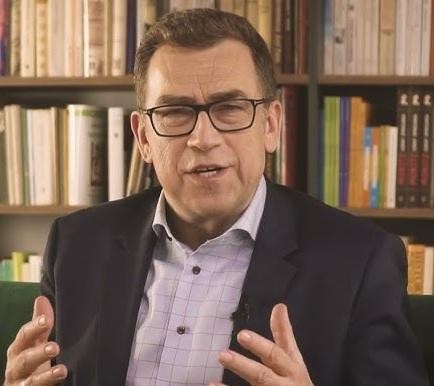Maciej Orłoś podczas dynamicznej prezentacji lub szkolenia z wystąpień publicznych, gestykulujący z energią, w nowoczesnej sali konferencyjnej.